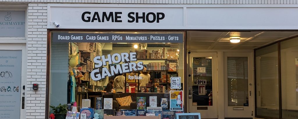 exterior of Shore Gamers storefront with signs that read "Game Shop, Board Games, Card Games, RPGs, Miniatures, Puzzles, Gifts"