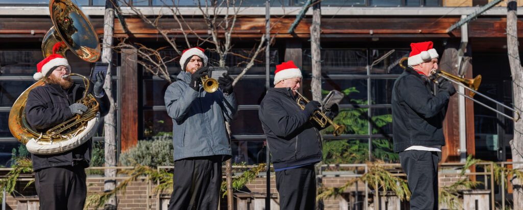 Four men wearing Santa hats playing brass instruments