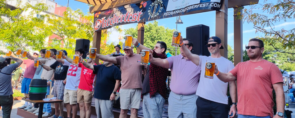 men holding up steins of beer under an Oktoberfest banner